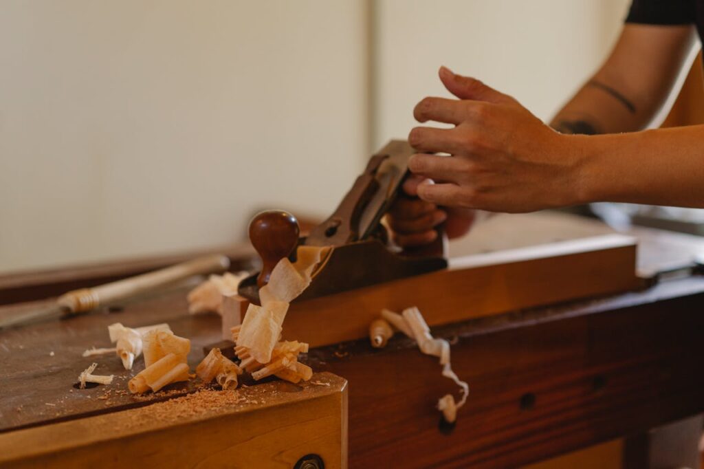 Crop joiner shaping hardwood plank with jack plane working at table in modern workshop
