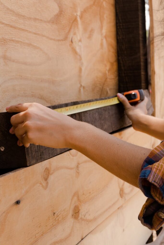 Hands measuring a wooden plank with a tape measure, capturing the essence of carpentry work.